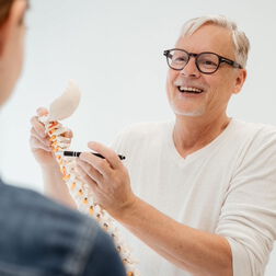 Dr. Burkhard Schubert zeigt einer Patientin an einem Modell der Wirbelsäule die Nerven-Austritte
