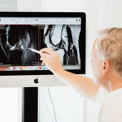 Dr. Burkhard Schubert betrachtet gemeinsam mit einer Patientin die MRT Aufnahme eines Knies am Computer