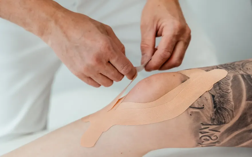 Dr. Burkhard Schubert klebt Tape auf beide Seiten des Knies einer Patientin
